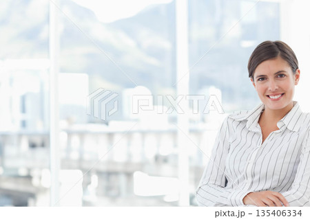 Female professional smiling while sitting in office chair at desk with glass windows, copy space 135406334