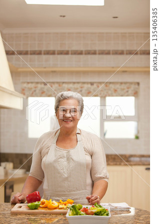Senior woman chopping bell peppers on wooden cutting board at marble countertop island in kitchen 135406385