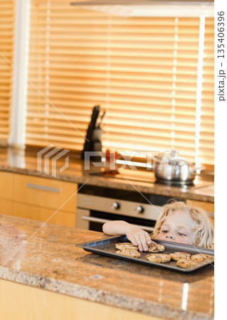 Preschool boy reaching for chocolate chip cookies on granite kitchen island with blinds, copy space Preschool boy reaching for chocolate chip cookies on granite kitchen island with blinds, copy space 135406396