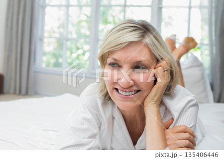 Woman lying on bed with white sheets wearing button-up shirt showing ring at multi-pane window Woman lying on bed with white sheets wearing button-up shirt showing ring at multi-pane window 135406446
