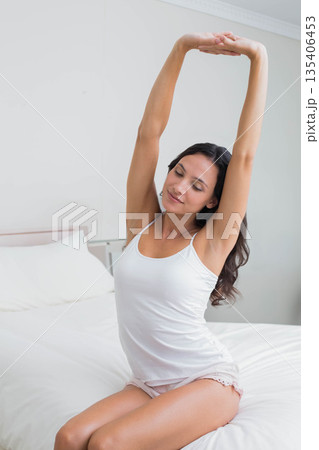 Woman stretching arms overhead on bed in bright bedroom with white duvet and pillows Woman stretching arms overhead on bed in bright bedroom with white duvet and pillows 135406453