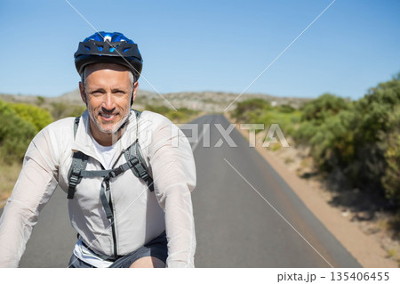Male cyclist gripping handlebars riding on paved road wearing blue helmet with backpack, copy space Male cyclist gripping handlebars riding on paved road wearing blue helmet with backpack, copy space 135406455