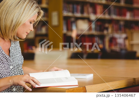 Woman reading open book and turning pages at library reading room wooden table, copy space Woman reading open book and turning pages at library reading room wooden table, copy space 135406467