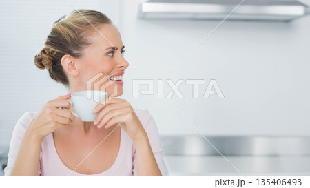 Mid adult woman standing in modern kitchen holding white mug near stainless range hood, copy space 135406493