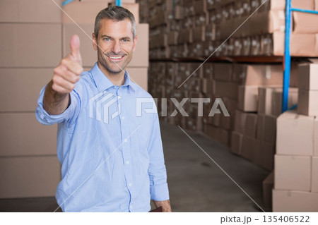 Man standing in storage facility giving thumbs-up holding clipboard near metal shelves and boxes 135406522