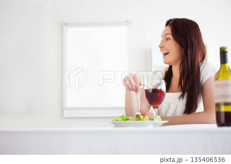 Woman sitting at dining table by window eating green salad with wine glass, copy space Woman sitting at dining table by window eating green salad with wine glass, copy space 135406536