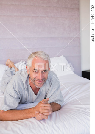 Senior man lying in bedroom on bed with white linens and headboard smiling toward camera Senior man lying in bedroom on bed with white linens and headboard smiling toward camera 135406552
