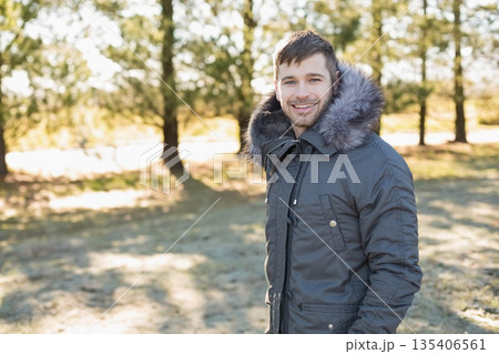 Man standing wearing winter coat under sunlit pine grove clearing, breathing chilly air, copy space Man standing wearing winter coat under sunlit pine grove clearing, breathing chilly air, copy space 135406561