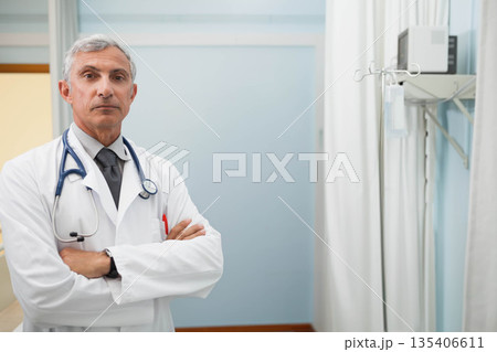 Middle-aged male doctor standing in hospital room near IV pole, monitor, stethoscope, copy space 135406611
