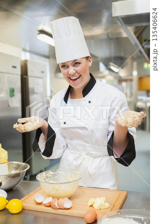 Female chef kneading dough with sticky hands at commercial kitchen counter with eggs and lemons Female chef kneading dough with sticky hands at commercial kitchen counter with eggs and lemons 135406624