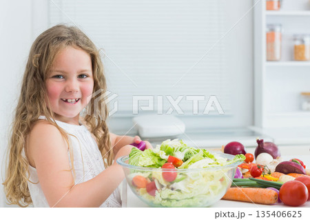 Female child holding peeler and chopping lettuce into salad bowl on kitchen countertop, copy space 135406625