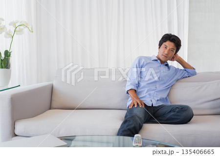 Japanese man sitting on gray sofa in bright living room with orchid and remote, copy space Japanese man sitting on gray sofa in bright living room with orchid and remote, copy space 135406665