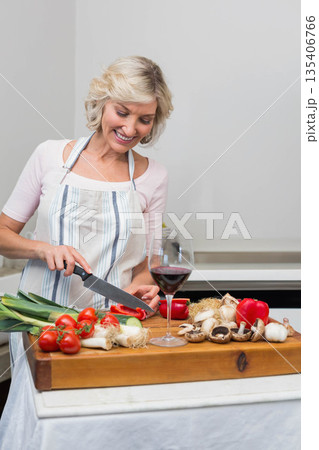 Middle-aged woman slicing bell pepper with chef's knife on wooden cutting board next to wine glass Middle-aged woman slicing bell pepper with chef's knife on wooden cutting board next to wine glass 135406766