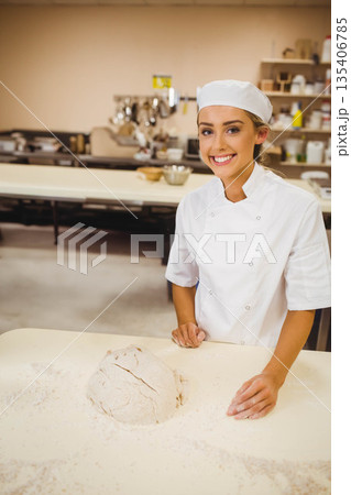 Female chef smiling behind worktable in bakery kitchen, kneading dough in chef uniform, copy space 135406785