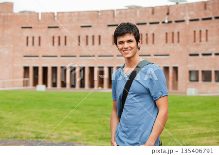 Male student smiling on lawn at campus carrying dark shoulder bag in front of brick columns Male student smiling on lawn at campus carrying dark shoulder bag in front of brick columns 135406791