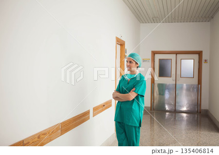 Woman wearing green surgical scrubs and mask standing at handrails in hospital corridor, copy space 135406814