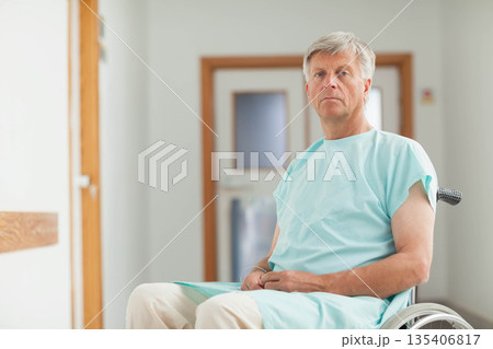 Senior man sitting in wheelchair wearing gown in ward corridor with handrail, door, copy space Senior man sitting in wheelchair wearing gown in ward corridor with handrail, door, copy space 135406817