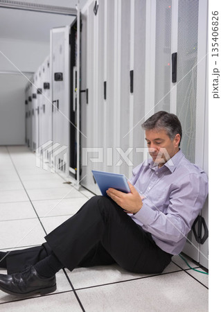 IT professional man sitting on data center floor tiles inspecting equipment with tablet, copy space 135406826