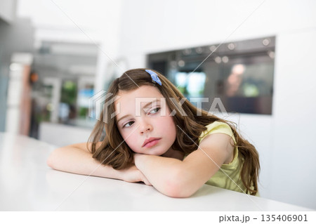 Child girl leaning on white kitchen countertop, wearing blue hair clip, gazing thoughtfully aside Child girl leaning on white kitchen countertop, wearing blue hair clip, gazing thoughtfully aside 135406901