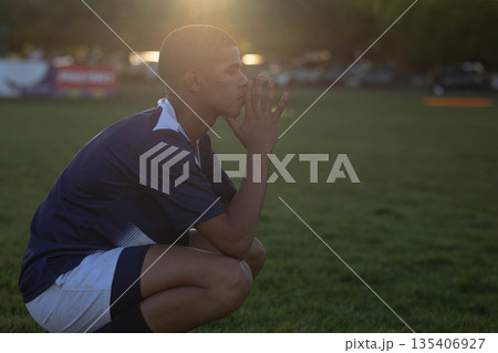 African American teenage male athlete crouching on grass field wearing sports jersey and shorts African American teenage male athlete crouching on grass field wearing sports jersey and shorts 135406927