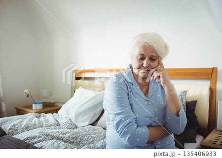 Senior woman sitting on bed edge in bedroom with patterned duvet wearing heart print pajamas Senior woman sitting on bed edge in bedroom with patterned duvet wearing heart print pajamas 135406933
