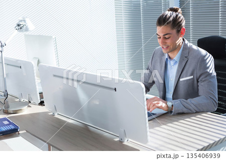 Man in grey suit typing on laptop behind white privacy panel in open-plan office, copy space Man in grey suit typing on laptop behind white privacy panel in open-plan office, copy space 135406939