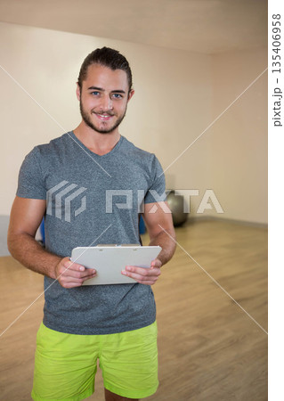Male instructor holding clipboard while guiding workout in fitness studio with exercise ball Male instructor holding clipboard while guiding workout in fitness studio with exercise ball 135406958