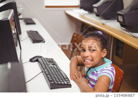 African American school-aged girl typing on keyboard and smiling at camera in computer lab 135406987