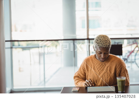 African American woman focusing on tablet while sitting at cafe with green smoothie, copy space African American woman focusing on tablet while sitting at cafe with green smoothie, copy space 135407028