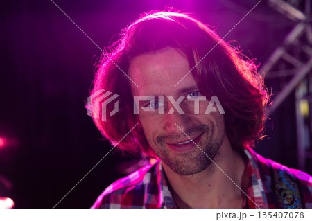 Mid-thirties man smiling and standing on stage under pink spotlights with metal lighting truss Mid-thirties man smiling and standing on stage under pink spotlights with metal lighting truss 135407078