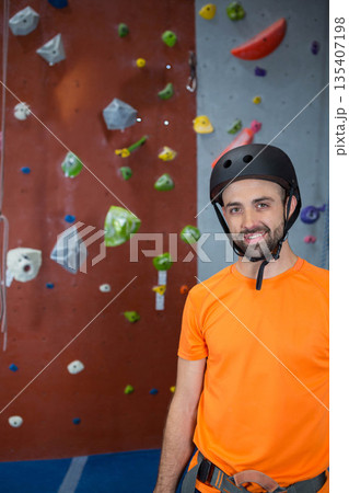White adult male climber wearing harness and helmet climbing wall in gym with holds, copy space 135407198