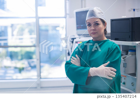 Senior woman surgeon wearing scrubs standing near anesthesia machine in surgical suite, copy space 135407214