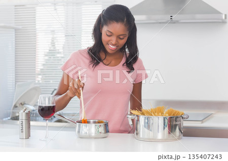 African American woman stirring sauce in saucepan on kitchen counter with pasta pot, pepper grinder African American woman stirring sauce in saucepan on kitchen counter with pasta pot, pepper grinder 135407243