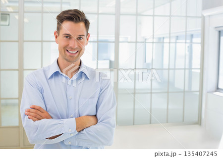 Man standing with arms crossed wearing blue shirt and trousers in office glass grid partition Man standing with arms crossed wearing blue shirt and trousers in office glass grid partition 135407245