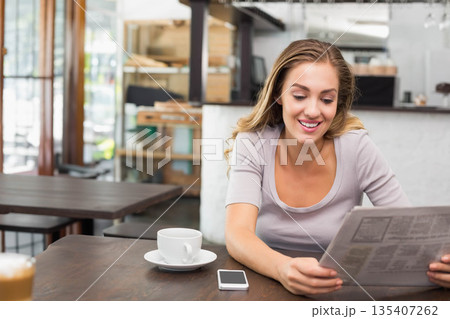 Woman reading newspaper at wooden cafe table holding coffee cup and smartphone, copy space Woman reading newspaper at wooden cafe table holding coffee cup and smartphone, copy space 135407262