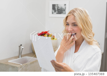 Woman in late twenties holding document and gasping in kitchen by framed photograph, copy space Woman in late twenties holding document and gasping in kitchen by framed photograph, copy space 135407369