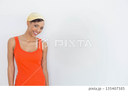 African American woman standing in orange tank top, yellow bandana against white wall, copy space African American woman standing in orange tank top, yellow bandana against white wall, copy space 135407385