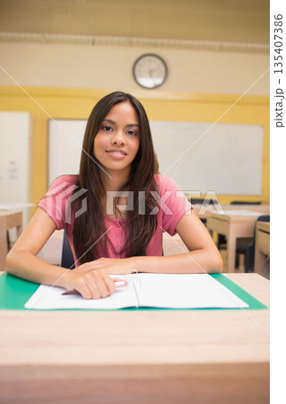 Female student sitting at wooden desk in classroom reviewing notes in open binder under clock Female student sitting at wooden desk in classroom reviewing notes in open binder under clock 135407386