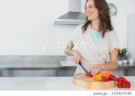 Woman slicing red and yellow bell peppers on wooden cutting board at kitchen counter, copy space Woman slicing red and yellow bell peppers on wooden cutting board at kitchen counter, copy space 135407540
