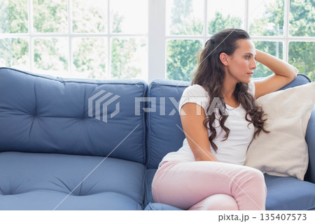 Woman sitting on blue sofa at home leaning gazing through window with green foliage, copy space 135407573