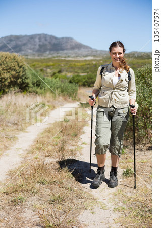 Woman hiking on dry hillside trail wearing jacket with trekking poles and backpack, copy space Woman hiking on dry hillside trail wearing jacket with trekking poles and backpack, copy space 135407574