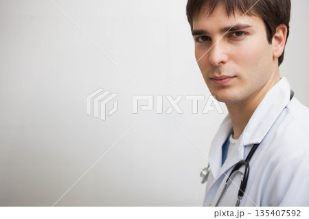 male doctor standing against clinic wall wearing stethoscope and white lab coat, copy space 135407592