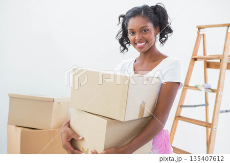 African American woman carrying moving boxes in bare room with wooden stepladder and small tools 135407612