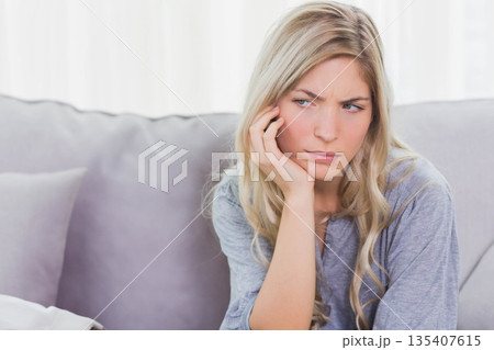 Woman sitting on sofa at home leaning head on hand with cushion near curtains, copy space 135407615