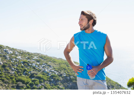 Man in his 30s standing on coastal hillside exercising with blue water bottle, copy space Man in his 30s standing on coastal hillside exercising with blue water bottle, copy space 135407632