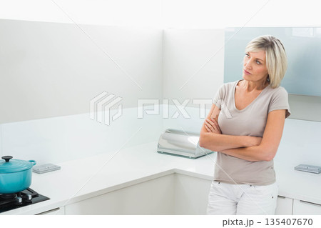 Woman wearing beige T-shirt standing at stovetop cooking with turquoise pot in kitchen, copy space 135407670