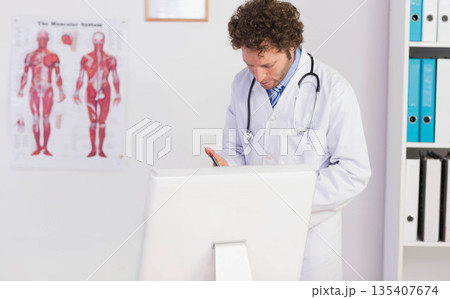 Male doctor wearing stethoscope writing notes on clipboard in clinic with chart, copy space 135407674