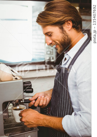 Adult male barista locking portafilter on espresso machine and pulling shot into cup behind counter 135407692