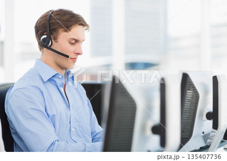 Male customer support agent wearing blue shirt working in office with headset, monitors, copy space Male customer support agent wearing blue shirt working in office with headset, monitors, copy space 135407736