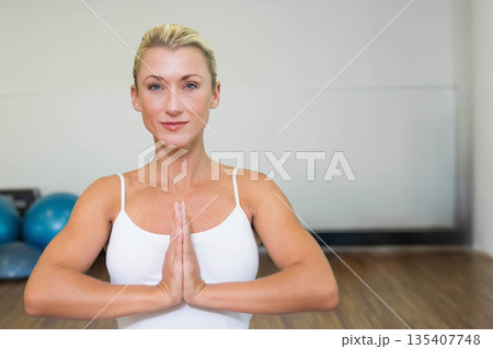 Female practicing prayer pose at fitness studio with blue stability balls on wooden floor Female practicing prayer pose at fitness studio with blue stability balls on wooden floor 135407748